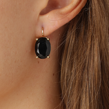 Black gemstone earring on a person's ear with gold setting