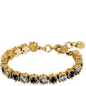 A gold-plated tennis bracelet featuring alternating round black and clear crystals in prong settings, complete with a lobster clasp and a branded tag.
