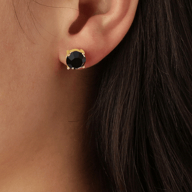 Close-up of an ear wearing a gold earring with a black gemstone.