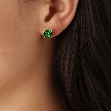 Close-up of an ear wearing a gold earring with a green gemstone.