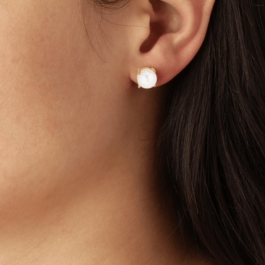 Close-up of an ear wearing a gold earring with a white gemstone.