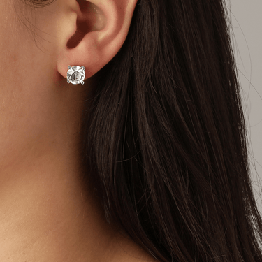 Close-up of an ear wearing a diamond earring with dark hair and skin background