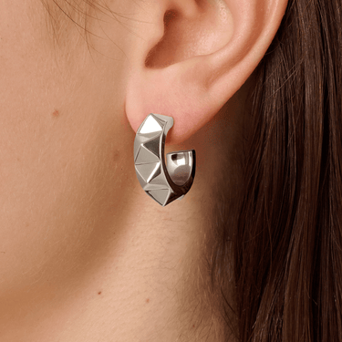 Silver geometric hoop earring worn by a person with brown hair.