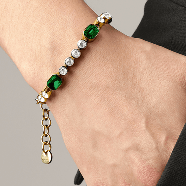 Bracelet with green and clear gemstones on a wrist against a neutral background