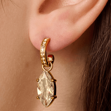 Gold earring with a clear gemstone worn on an ear