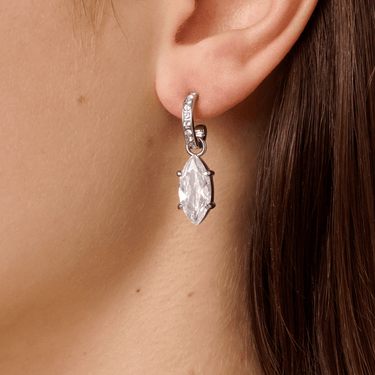 Close-up of a silver earring with a marquise-shaped gemstone worn by a person.