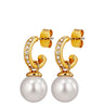 A pair of gold huggie hoop earrings with small clear rhinestones and a large white pearl drop, shown on a plain white background.