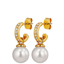 A pair of gold huggie hoop earrings with small clear rhinestones and a large white pearl drop, shown on a plain white background.
