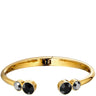 A polished gold open cuff bracelet featuring three bezel-set round black gemstones, shown against a solid white background.
