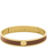 A gold-tone metal hinged bangle bracelet with a smooth brown inlay band and a circular gold-tone logo medallion on the front, set against a plain white background.