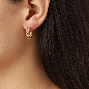 Close-up of a person wearing a gold hoop earring with small stones.