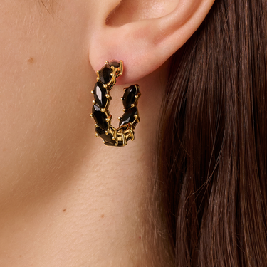 Gold hoop earrings with black stones worn by a person with long brown hair.