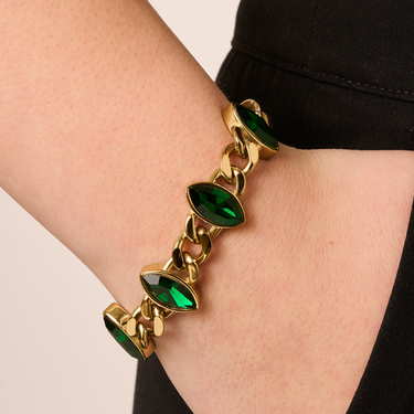 Gold bracelet with green gemstones on a wrist against a neutral background