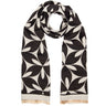A black and off-white scarf with a repeating geometric leaf pattern, draped in a loop to show its length and fringed ends against a plain white background.