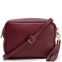 A burgundy pebbled leather crossbody bag with a matching leather tassel charm and gold-tone hardware, shown on a clean white background.