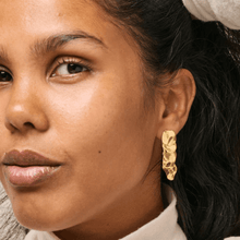 Close-up of a woman wearing gold earrings with a neutral background