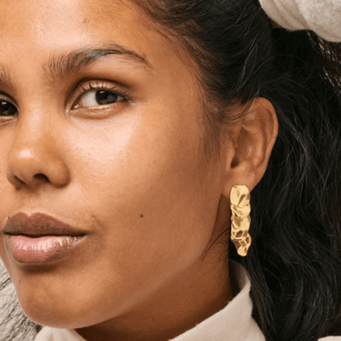 Close-up of a woman wearing gold earrings with a neutral background