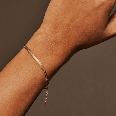 Gold bracelet with a small green gemstone on a wrist against a brown background