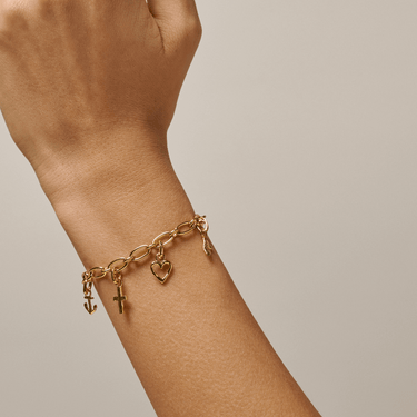 Gold bracelet with charms on a wrist against a neutral background