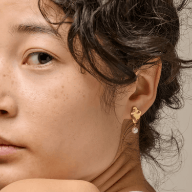 Close-up of a person wearing a gold earring with a pearl detail.