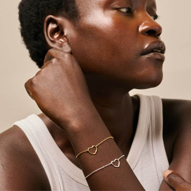 Woman wearing gold heart-shaped bracelets on a neutral background
