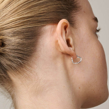 Close-up of a person wearing a silver hoop earring on a neutral background