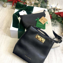 Black handbag with gold clasp on a light wooden surface with Christmas decorations.