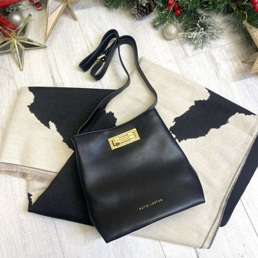 Black handbag with gold clasp on a decorative surface with Christmas decorations.