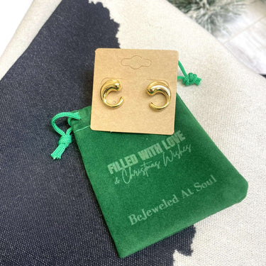 Gold earrings on a green card with text, placed on a textured surface.