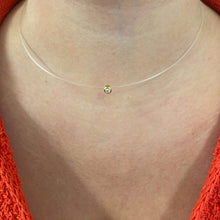 Necklace with a small round pendant on a person wearing an orange garment.