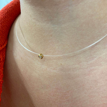 Clear necklace with a gold clasp on a person's neck against an orange background