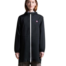 A woman wearing a black hooded raincoat with a white front zipper and a small circular red, white, and blue logo on the left chest, photographed against a plain white studio background.