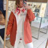 Person taking a mirror selfie wearing a coral jacket and white pants in a store.