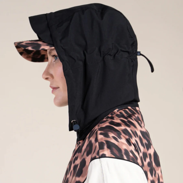 Person wearing a black hooded jacket over a leopard print outfit on a beige background