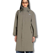 A woman wearing a mid-length olive green hooded raincoat with a high collar, snap-button front, and side pockets, photographed against a plain white background.