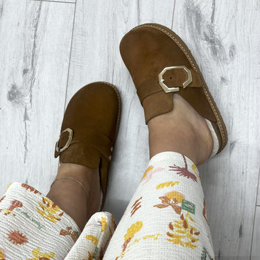 Brown suede shoes with buckles worn on a light wooden floor.