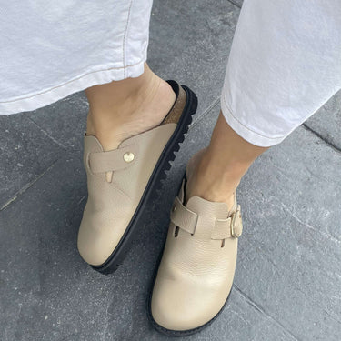 Beige clogs worn on a stone pavement