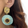 Close-up of a gold and light blue earring worn by a person with brown hair.