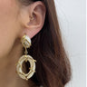 Close-up of a person wearing gold and white earrings with a plain background
