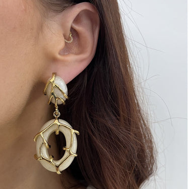 Close-up of a person wearing gold and white earrings with a plain background