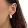 Close-up of an ear wearing a gold and white hoop earring with brown hair.