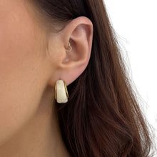 Close-up of an ear wearing a gold and white hoop earring with brown hair.