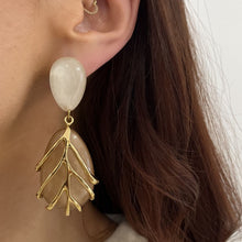 Close-up of a woman's ear wearing a gold and beige leaf-shaped earring.