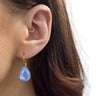 Close-up of an ear wearing a blue teardrop earring with a gold hoop.