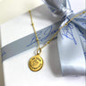 Gold necklace with a pendant on a white box with blue ribbon