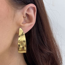 Gold earring worn by a person with a plain background