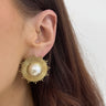 Gold earring with pearl center worn by a person with brown hair.