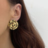 Gold circular earring worn by a person with a neutral background
