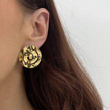 Gold circular earring worn by a person with a neutral background