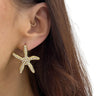 Gold starfish earring worn by a person with brown hair.